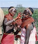 Samburu girls paint each others faces with abstract designs in readiness for a dance. Already,their necks and beaded necklaces have been coated with red ochre. Only girls and warriors decorate their faces; the orange powder they use is called blue.