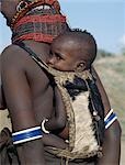 When a Turkana woman gives birth,four goats will be slaughtered in a twenty-four-hour period to celebrate the occasion. The skin of the first goat will be made into a pouch for carrying the baby on its mother's back. The small wooden balls on the back of this pouch are charms to ward off evil spirits. The baby is wearing a bracelet of ostrich eggshell beads.