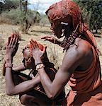 A Maasai warrior resplendent with long ochred braids tied in a pigtail at the back,puts red ochre on his friend's plaits. Red ochre is anatural earth,which is mixed with animal fat to the consistency of greasepaint.