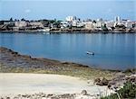 Kenya,Coast,Mombasa. A fisherman in a dugout canoe paddles past Fort Jesus and the old town of Mombasa. Only dhows - the wooden sailing vessels of the region - now use the Old Harbour.