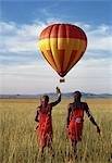 Two Maasai warriors watch a hot air balloon flight over Masai Mara.