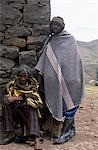 Lesotho men wrap themselves in woollen blankets to keep warm outside a stone shelter.