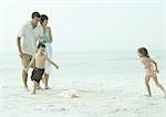 Family at the beach, children running around beach mat