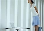Woman standing on chair, looking down at laptop