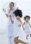 Two little girls running around bride on beach