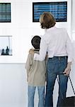 Woman and boy looking at arrival and departure boards in airport, rear view