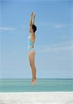 Woman jumping on beach, side view