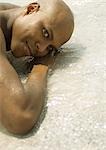 Man lying in shallow water on beach, looking at camera