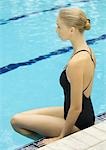 Femme assise sur le bord de la piscine avec les pieds dans l'eau, vue latérale