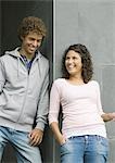 Young man and woman, leaning against corner of wall, laughing