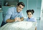Father and daughter standing by counter with flour sprinkled on it, heart drawn in flour