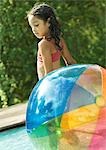 Jeune fille debout dans la piscine, avec ballon de plage