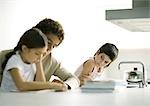 Teenage boy helping younger sister with homework, second sibling watching