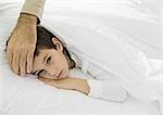 Child lying in bed with father's hand on forehead