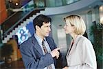 Male and female business associates standing in lobby, man pointing at woman