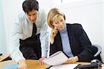 Business colleagues, man leaning over woman's shoulder, pointing to documents