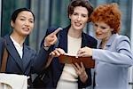 Three businesswoman looking at agenda, one pointing out of frame