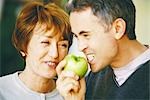 Senior man eating apple, senior woman laughing, close-up