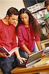 Two young adults looking at laptop, one holding user's manual