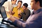 Three young men using electronic organizer, laptop user in foreground