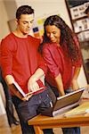 Young man and woman standing next to laptop, man pointing to user's manual