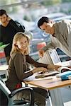 Office scene, man leaning toward female colleague, both smiling at camera