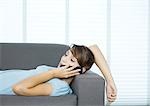 Young woman lying on couch, using cell phone