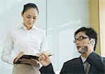 Businessman and female assistant, man using phone and gesturing to agenda