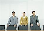 Business executives standing with hands on backs of chairs in conference room