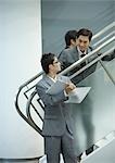 Businessman standing on stairs, looking down at file held by associate