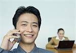 Businessman using cell phone, colleague working in background, portrait