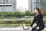Businesswoman using laptop by water in office park