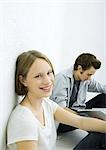 Teenage girl and young man sitting on floor, girl smiling at camera