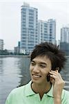 Young man using cell phone by river