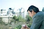 Businessman holding cup, city in background