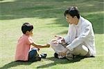 Father and son sitting on grass playing "rock paper scissors"