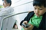 Boy using cell phone while father sits with eyes closed