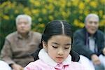 Girl looking down, grandparents in blurred background