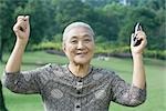 Senior woman raising arms, holding cell phone