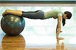 Young woman doing push-ups with legs resting on fitness ball
