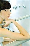 Woman sitting in weight room, holding on to metal bar, looking away