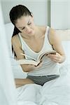 Jeune femme assise sur le lit, livre de lecture