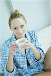 Woman wearing nightshirt, holding cup of tea, smiling at camera