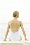 Teenage girl sitting, wearing bathing suit, rear view