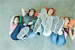 Four teen friends lying on backs on floor, holding up legs, focus on soles of shoes