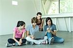 Four teen friends sitting on floor together, using laptop