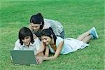 Young friends lying in grass, using laptop together