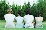 Quatre jeunes amis assis sur l'herbe, côte à côte, vue arrière