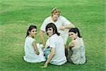 Four young friends sitting on grass, looking at camera