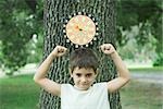 Boy standing in front of dart board on tree, arms up